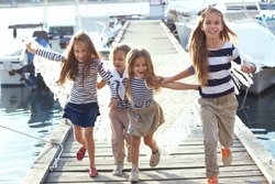 Group of 4 fashion kids wearing same striped navy clothes in marine style running in the sea port