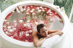 Woman relaxing in round outdoor bath with tropical flowers, organic skin care, luxury spa hotel, lifestyle photo, top view