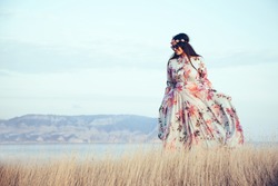 Plus size model wearing floral maxi dress posing in field. Young and fashionable overweight woman walking on the shore.
