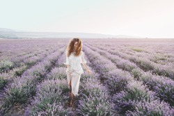 Beautiful model walking in spring or summer lavender field in sunrise backlit. Boho style clothing and jewelry.