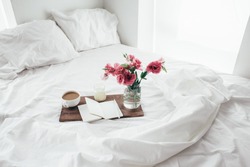 Wooden tray with paper sketchbook, candle and spring flowers on clean white bedding. Good morning concept.