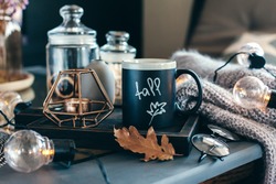 Still life details of living room. Cup of coffee on rustic wooden tray, candle and warm woolen sweater on table, decorated with led lights. Autumn weekend concept. Fall home decoration.