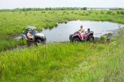 Adventures for adults - a trip on ATVs on not passable rural roads. Tourists on ATV in protective helmets from strikes and dirt, participate in the off-road race in the forest on a hot summer day.