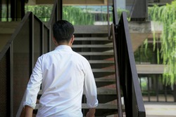 Back view of businessman walking up staircase. Back to office or climbing up the corporate ladder concept,