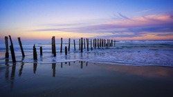 Old jetty posts at beautiful sunrise on St Clair Beach, Dunedin, Otago, South Island, New Zealand.
