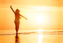 Lady's silhouette with raised arms against calm sunset beach