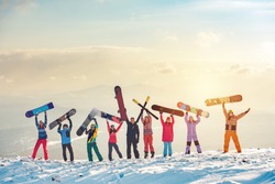 Big group of happy friends skiers and snowboarders having fun and holding ski and snowboards on mountain top