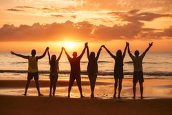 Group of happy friends are having fun with raised arms together at sea beach and enjoy sunset