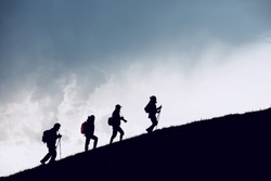 Group of four hikers silhouettes are going uphill in mountains against cloudy sky