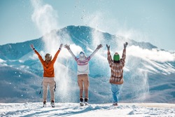 Three happy adult girls are having fun and throws first snow on background of mountains. Travel in winter time concept