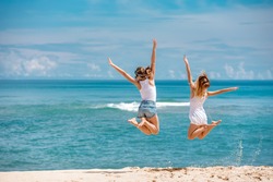 Two young girls are jumping on background of blue sea