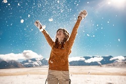 Happy young girl is tossing the snow in mountains. Winter vacations concept