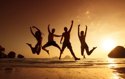 Young friends having fun on the beach and jumping against a backdrop of a sunset over the sea. Phranang beach, Krabi province, Thailand