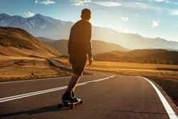Man rides at straight road on longboard at sunset time