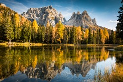 autumn colorful dolomites mountain peaks in italy with blue sky reflecting in the lake