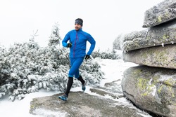 young man in blue sportswear running on the snow frozen trail in winter mountains with cold fog