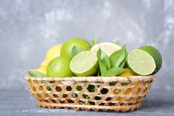 Lemons and limes with green leafs in basket on grey wooden table