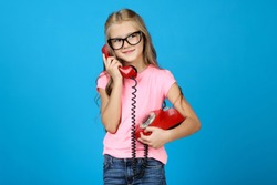 Beautiful little girl with handset and telephone on blue background