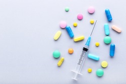 Colorful pills with syringe on grey background