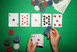 Female hand holding cards with poker chips and dollar banknotes on green table