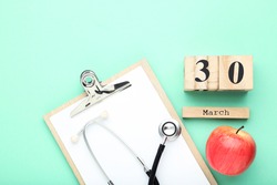 Stethoscope with clipboard, red apple and cube calendar on mint background