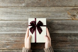 Female hands holding gift box on grey wooden background