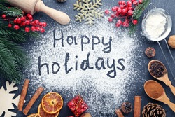 Inscription Happy Holidays on wheat flour background with fir-tree branches, orange fruits and cones