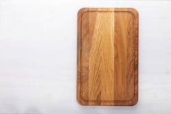 Rectangular cutting board on a white wooden table. Food preparation tool and kitchen utensils. Space for text.