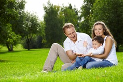 Mother, father and small son have a rest on lawn in summer park