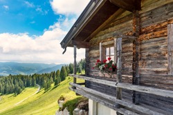 Idyllic alpine wooden mountain hut scenery in Austrian alps, forest trees and  green meadows, sunny day, blue sky
