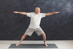 Sporty elderly guy practicing yoga indoors. Senior man doing stretching exercise, black background. Active lifestyle and healthcare in any age, copy space