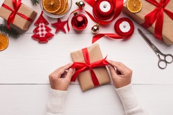 Woman is packing surprise gift for Christmas holidays, sitting at workplace with craft tools, top view