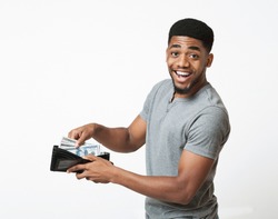 Finance, investment and money saving. Excited african-american man putting banknotes into wallet, white studio background
