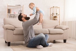Father and kid spending time together, man throwing up his son at home in living room, copy space