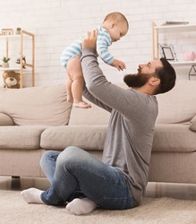 Happy young father lifting cute baby up high in air, spending and enjoying time together with son