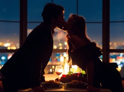 Loving couple kissing on panoramic window background with nigth urban view. Romance in the sky concept