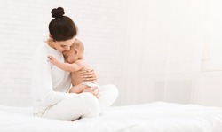 Young mother holding her newborn child, lulling baby in bed, copy space