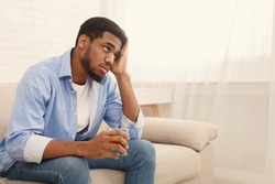 Loneliness. Young african american guy drinking alcohol at home alone, thinking about problems with glass of whiskey, free space