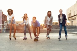 Cool teen friends. Happy teenagers having fun, riding on skateboards and rollers on summer evening