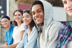 Multiethnic teen company spending time together, sitting outdoor, free space
