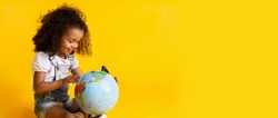 Early education. Little girl pointing to world globe, yellow background, copy space
