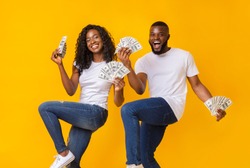 African american cheerful couple dancing with money in their hands, lifting legs up