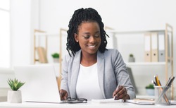 Smiling Afro Businesswoman Working On Laptop And Taking Notes In Modern Office. Free Space
