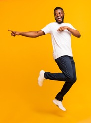 Joyful black millennial guy jumping on air and pointing aside, free space