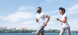 African American Couple Jogging Outdoor Along River Embankment Early In The Morning. Panorama, Free Space