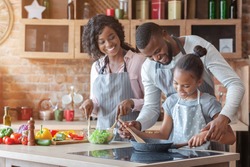 Kind african parents teaching their adorable daughter how to cook healthy food, free space