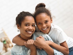 Two cute african american sisters hugging each other at home