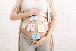 Choosing baby name. Confused pregnant woman with question marks on paper stickers on tummy