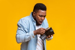 Where's my money. Shocked african american guy holding wallet with dollar cash that will be not enough to cover spendings, yellow studio background.