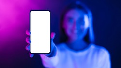 Woman showing phone with blank screen in neon lights, stretching cellphone to camera, free space